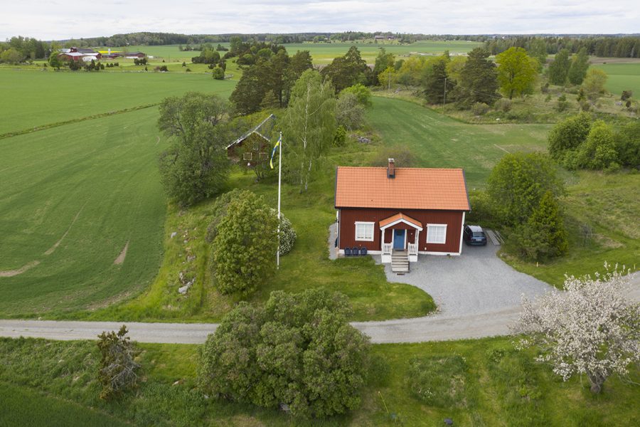 Ett litet rött hus mitt i ett odlingslandskap i mälardalen.