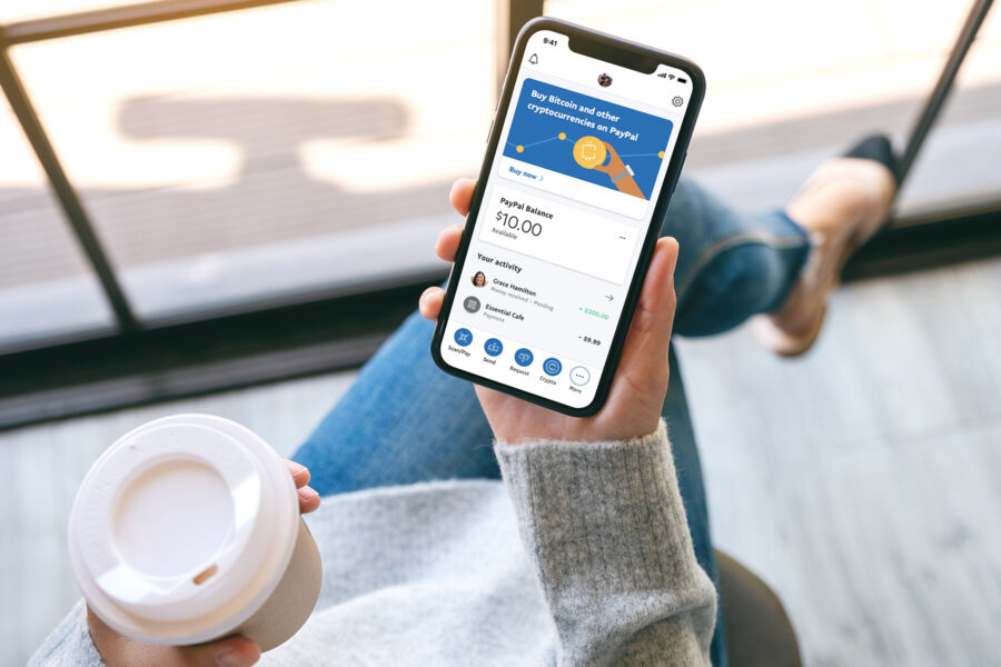 Paypal lanserar stablecoin - Paypal a woman holding a black mobile phone with blank white desktop screen with coffee cup