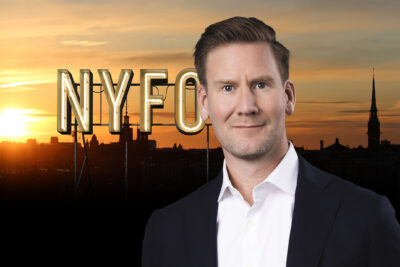 porträtt av en man i kostym och skjorta med en solnedgång över hustaken i bakgrunden