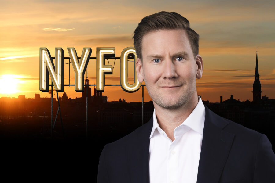 porträtt av en man i kostym och skjorta med en solnedgång över hustaken i bakgrunden