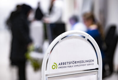 en skylt med texten arbetsförmedlingen och några personer i bakgrunden
