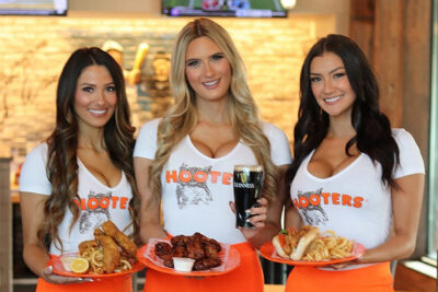 tre bystiga tjejer som håller i tallrikar med Hooters snabbmat