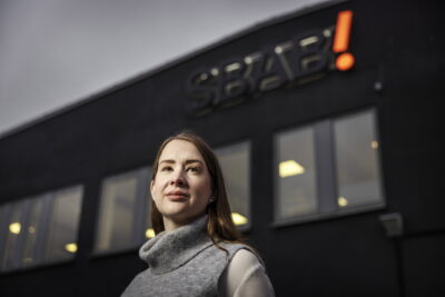 Linda Hasselvik, boendeekonom på SBAB framför en stor mörk byggnad